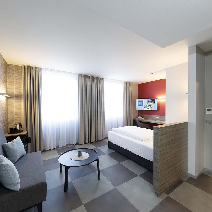 Median Hotel in Lehrte – wir geben Raum Modernes Hotelzimmer mit Sofa, Bett und angrenzendem Bad
