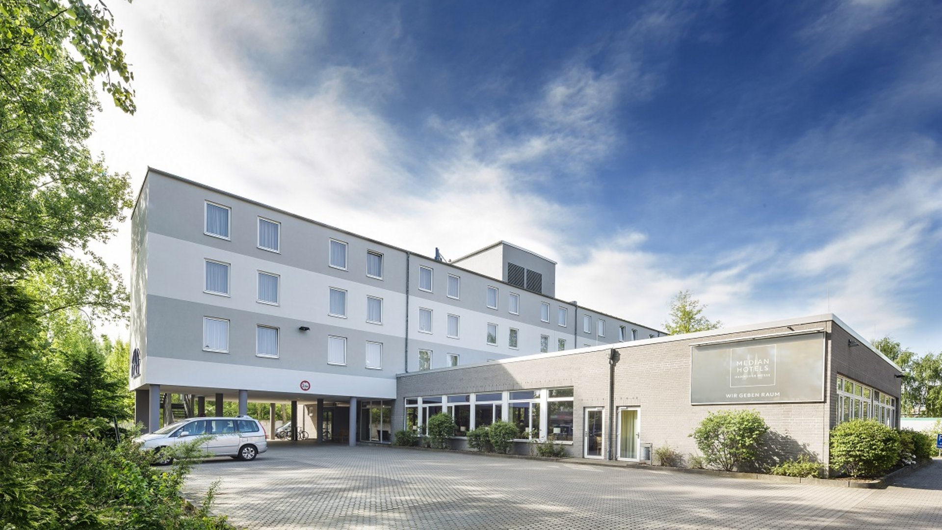 Willkommen im Median Hotel Hannover Messe! Außenansicht eines modernen Hotels mit Parkplatz und bewachsenem Gelände