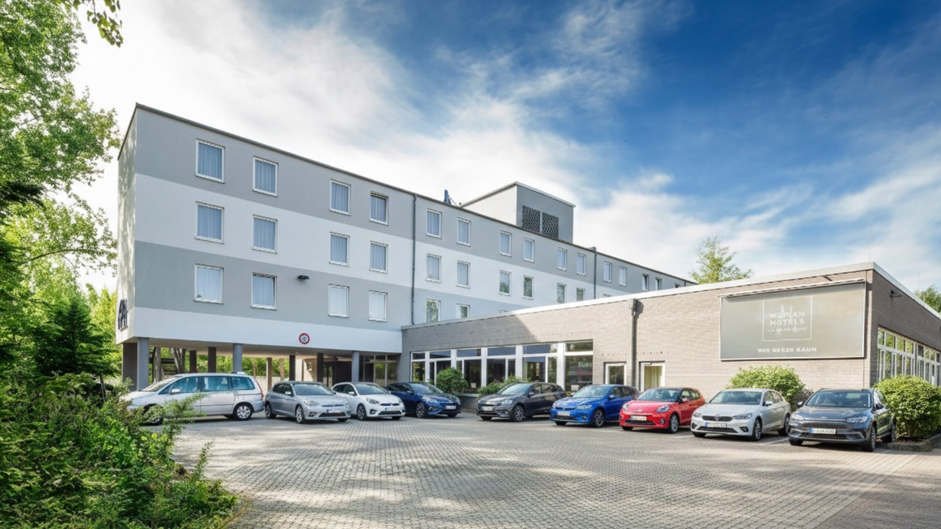 Willkommen im Median Hotel Hannover Messe! Vorderansicht eines Hotels mit parkenden Autos und blauem Himmel