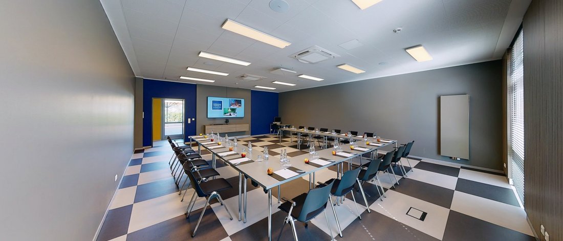 Ihr Tagungshotel in Hannover Moderner Konferenzraum mit U-förmigen Tischen, Stühlen, Flachbildschirm und Wasserflaschen